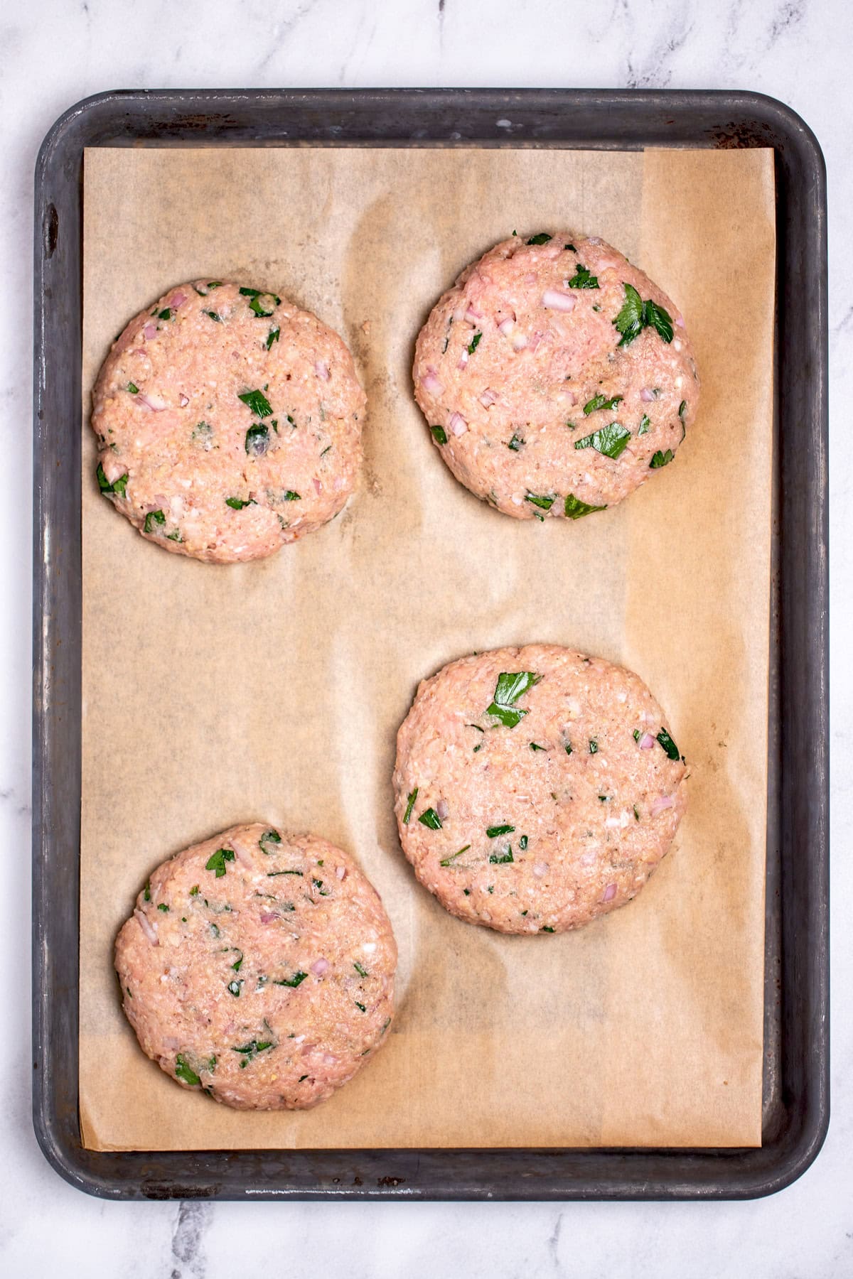 Four raw turkey burgers on a sheet pan lined with parchment paper.