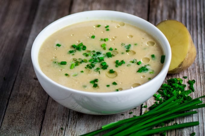 Potato leek soup in a white bowl on a wooden table, topped with chopped chives.