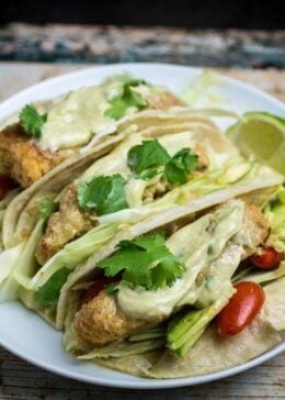 Crispy, juicy oven-fried fish smothered in a creamy, spicy avocado sauce and nestled in a warm tortilla. These Oven Fried Fish Tacos with Spicy Avocado Cream Sauce are simply perfect. Top with crunchy cabbage, cilantro, and a squeeze of fresh lime for an incredible flavor in this insanely easy-to-make dish!