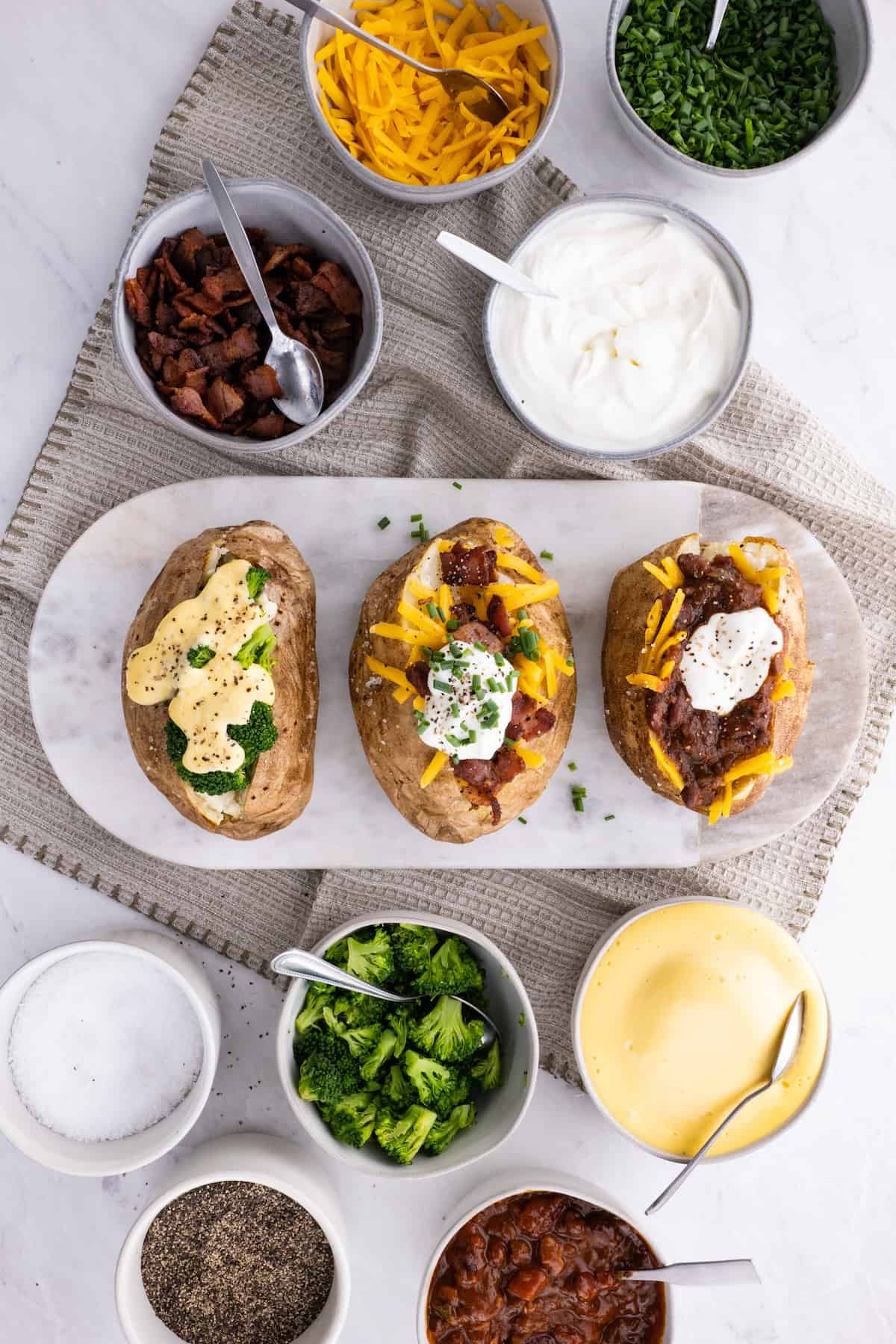 3 baked potatoes on a cutting board with cheese, bacon, and other toppings