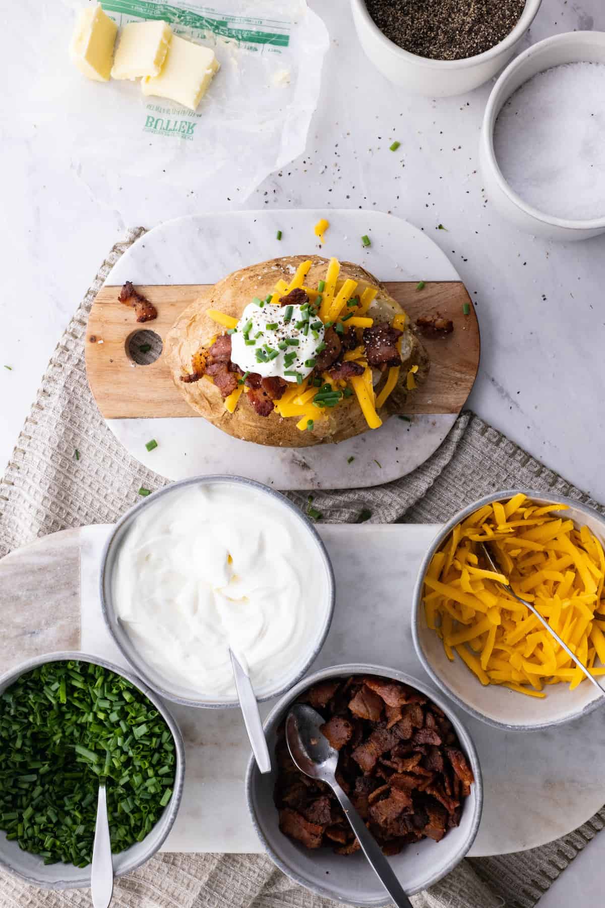 A baked potato on a cutting board with cheese, bacon, and other toppings