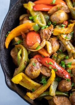 Half of a skillet with sausage, peppers, and onions fully cooked on a table.