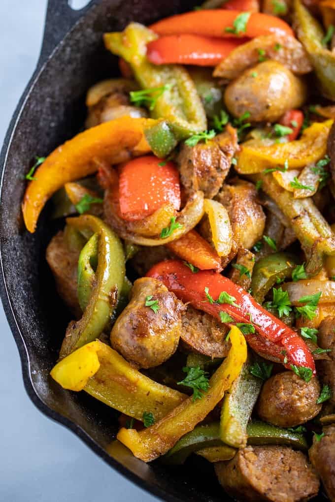 Half of a skillet with sausage, peppers, and onions fully cooked on a table. 