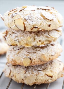 Side view of almond paste cookies stacked on top of each other with sliced almonds and powdered sugar