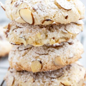Side view of almond paste cookies stacked on top of each other with sliced almonds and powdered sugar