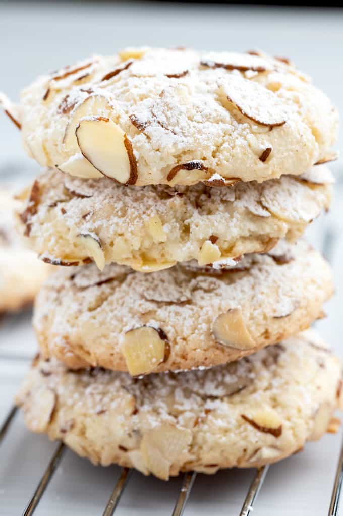 Side view of almond paste cookies stacked on top of each other with sliced almonds and powdered sugar