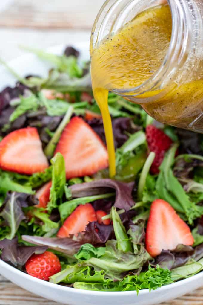 Poppy seed dressing drizzled from mason jar onto strawberry salad