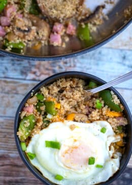 Bowl of country quinoa with an egg on top and skillet in the background