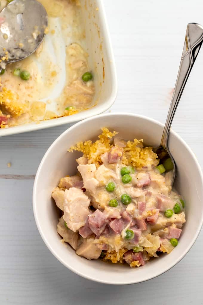 Downward shot of bowl of chicken cordon bleu casserole with spoon and casserole dish the the top left side