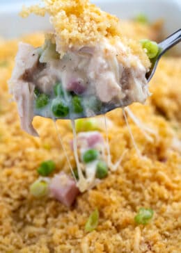 Spoon lifting up casserole portion from baking dish with stringy melted cheese