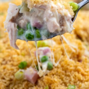 Spoon lifting up casserole portion from baking dish with stringy melted cheese