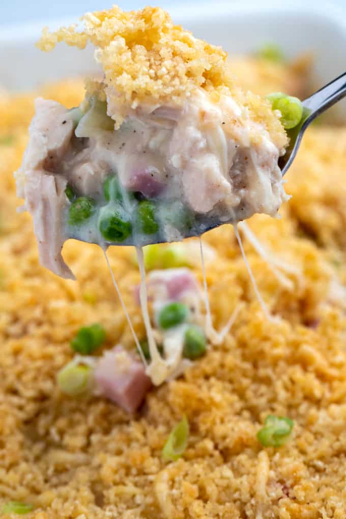 Spoon lifting up casserole portion from baking dish with stringy melted cheese