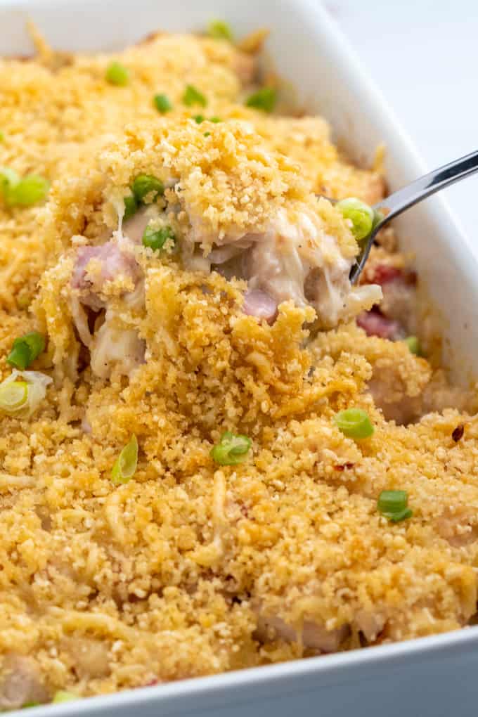 Spoon lifting up casserole portion from baking dish with melted cheese and crispy topping