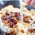 pecan cranberry baked brie photo from the side with stringy melted cheese on a cracker