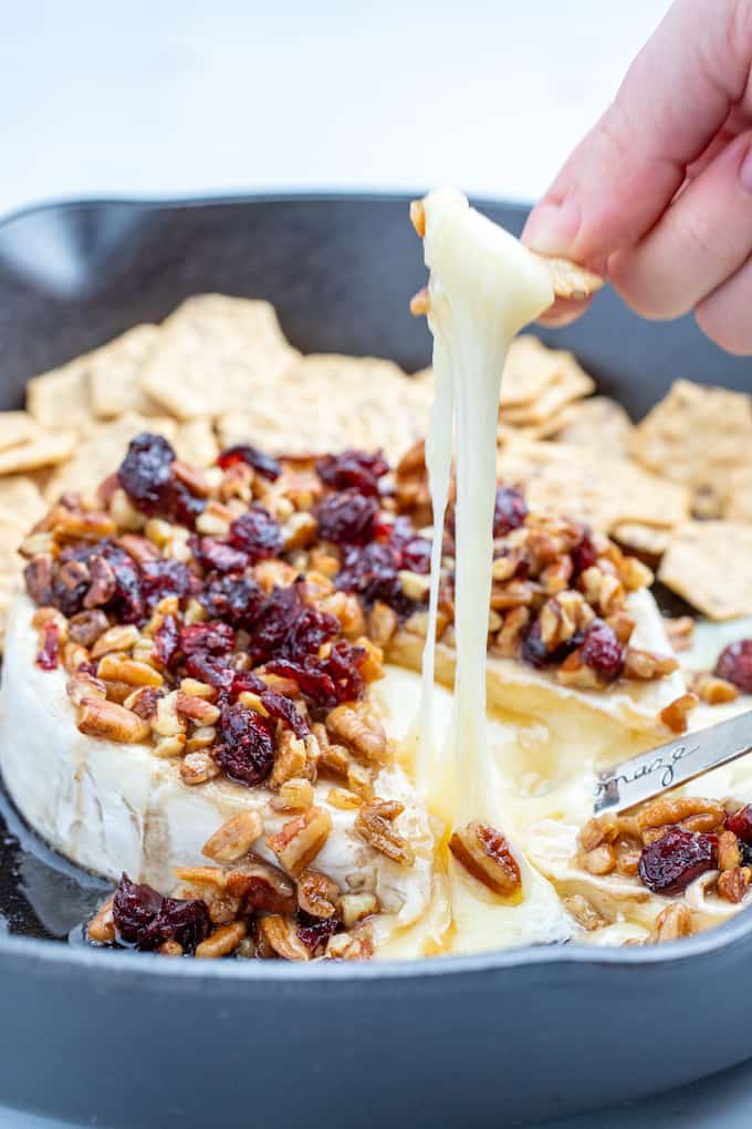 pecan cranberry baked brie photo from the side with stringy melted cheese on a cracker