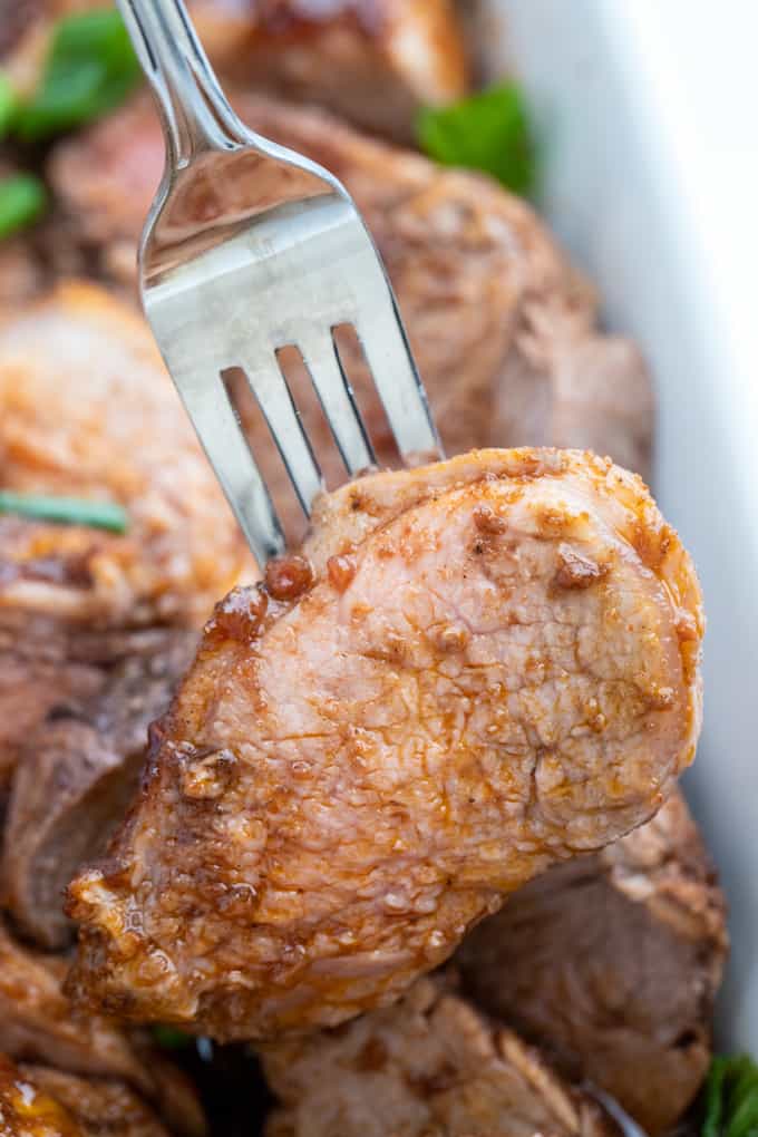 Pork tenderloin medallion on a fork with juicy liquid and raspberry balsamic marinade dripping from center 