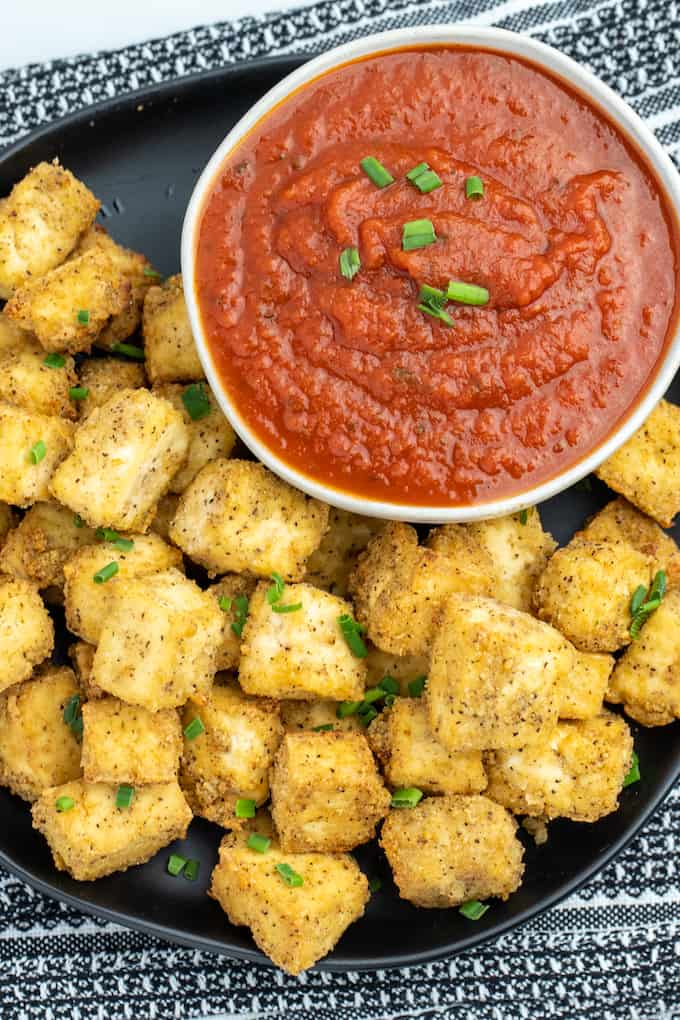 Overhead photo of air fried golden brown tofu cubes on a plate next to a bowl of marinara dipping sauce