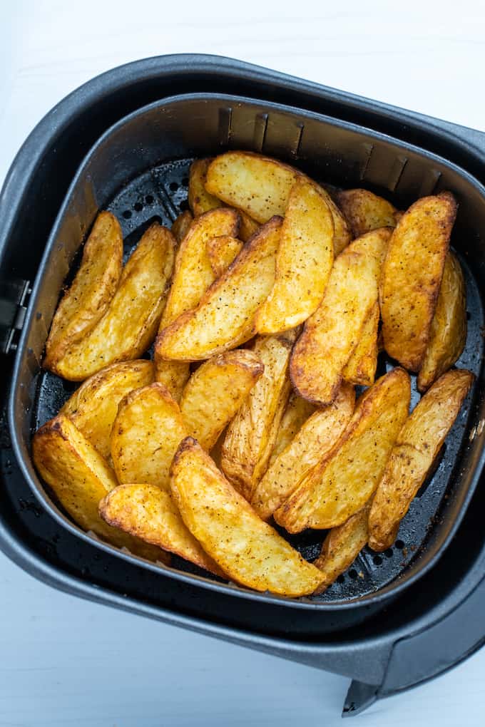 Overhead shot of air fryer basket full of crispy cooked potato wedges