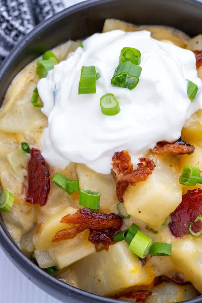 Top down view of a black bowl full of baked potato casserole topped with bacon, green onions, and sour cream.