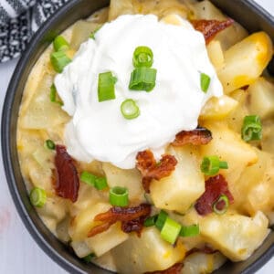 Top down view of a black bowl full of baked potato casserole topped with bacon, green onions, and sour cream.