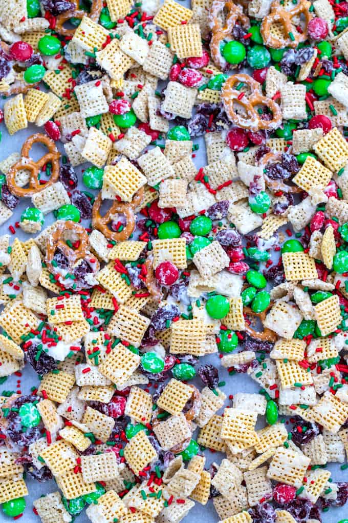 downward view of sheet pan with parchment paper and christmas chex mix made of pretzels, chex cereal, M&Ms, and dried cranberries coated in white chocolate