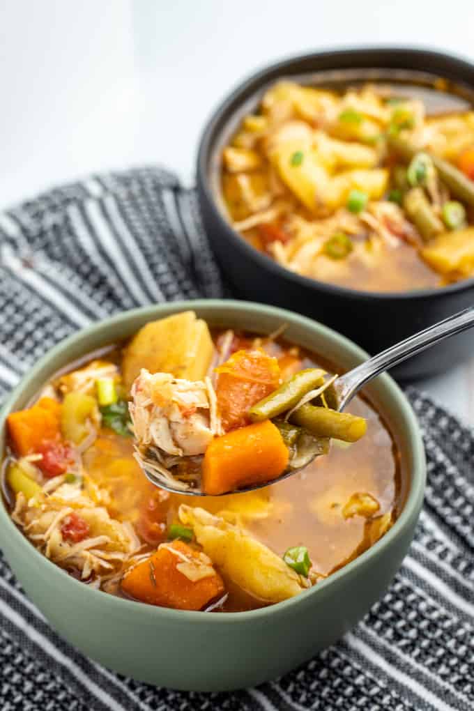 Two bowls of chicken stew on top of a kitchen town. The front bowl has a spoon in it. 