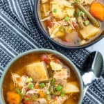 Top down shot of two bowls of chicken stew on top of a kitchen towel with a spoon to the right of the first bowl.