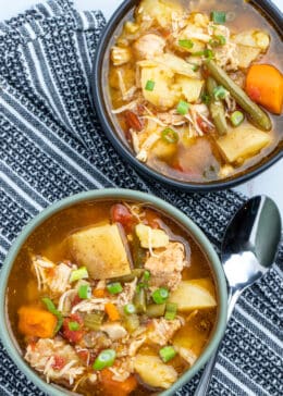 Top down shot of two bowls of chicken stew on top of a kitchen towel with a spoon to the right of the first bowl.