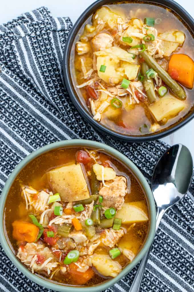 Top down shot of two bowls of chicken stew on top of a kitchen towel with a spoon to the right of the first bowl. 