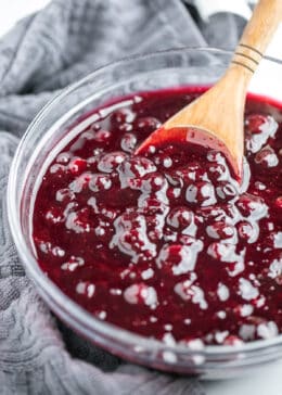 Wooden spoon scooping blueberry pie filling out of a glass bowl.