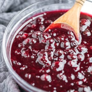 Wooden spoon scooping blueberry pie filling out of a glass bowl.