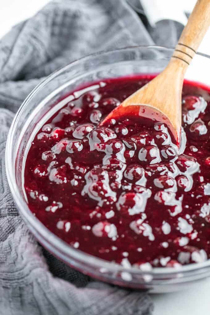 Wooden spoon scooping blueberry pie filling out of a glass bowl.