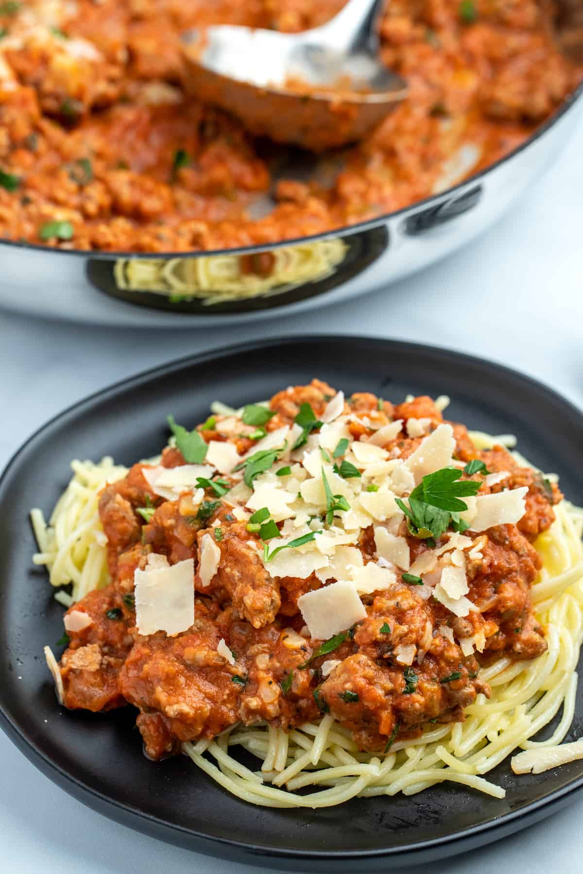 Turkey bolognese over gluten free pasta on a plate, next to a skillet of bolognese