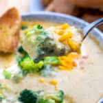 Bowl of broccoli cheddar soup with spoon full of soup topped with cheddar being held above the bowl