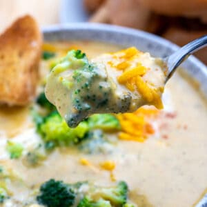 Bowl of broccoli cheddar soup with spoon full of soup topped with cheddar being held above the bowl