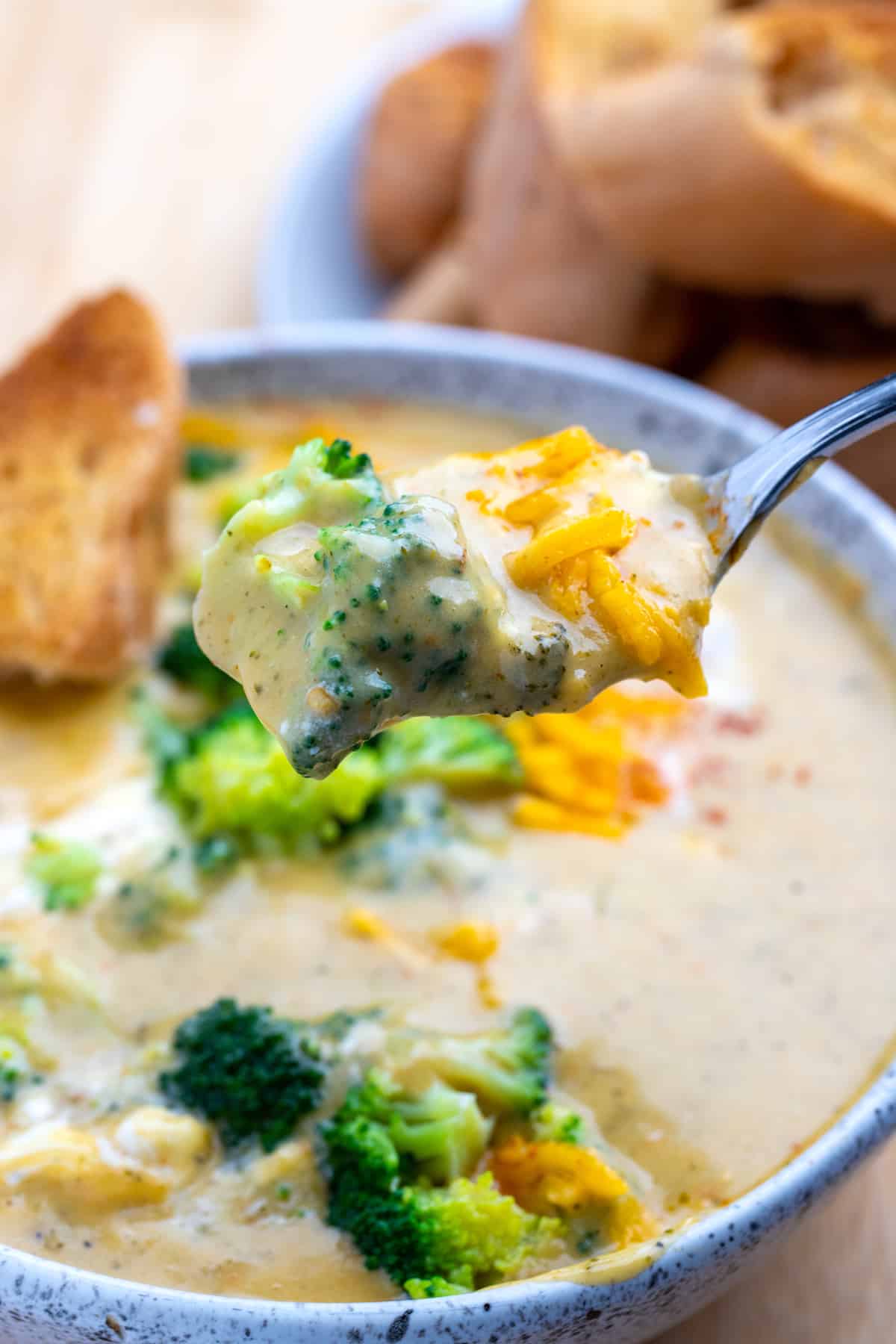Bowl of broccoli cheddar soup with spoon full of soup topped with cheddar being held above the bowl