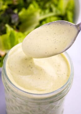 spoon and mason jar filled with avocado lime ranch dressing in front of a bowl of salad greens