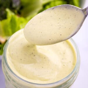 spoon and mason jar filled with avocado lime ranch dressing in front of a bowl of salad greens