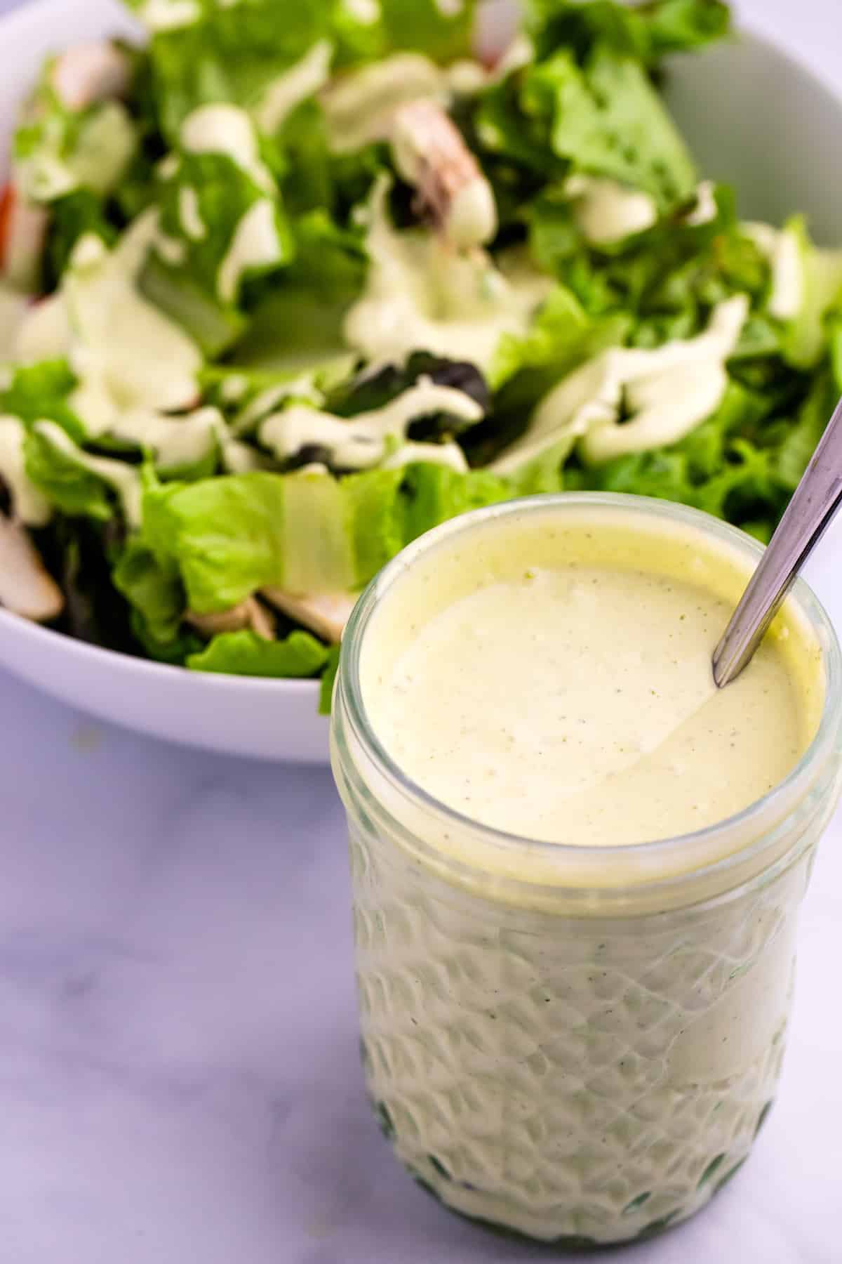 mason jar filled with avocado lime ranch dressing in front of a bowl of salad greens