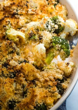 Broccoli and cauliflower in a cheesy sauce topped with breadcrumbs on a fork above the casserole dish.