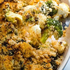 Broccoli and cauliflower in a cheesy sauce topped with breadcrumbs on a fork above the casserole dish.