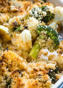 Broccoli and cauliflower in a cheesy sauce topped with breadcrumbs on a fork above the casserole dish.