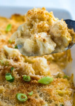 A spatula lifting cauliflower au gratin out of the baking dish.