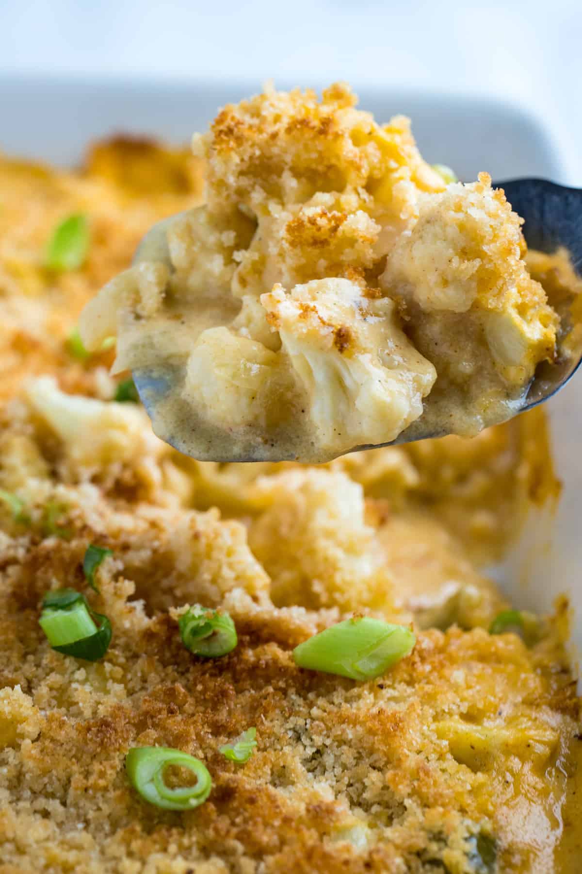 A spatula lifting cauliflower au gratin out of the baking dish.