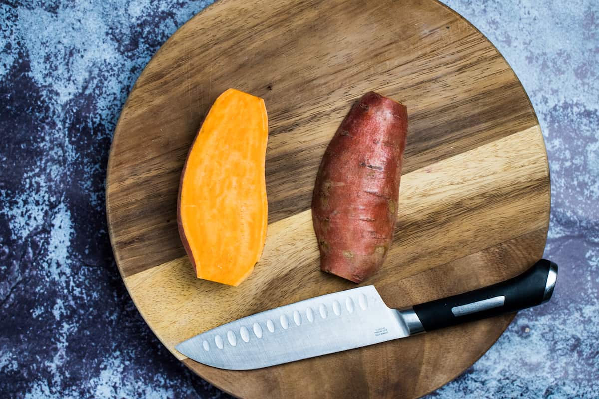 Sweet potatoes cut in half on a cutting board next to a knife.