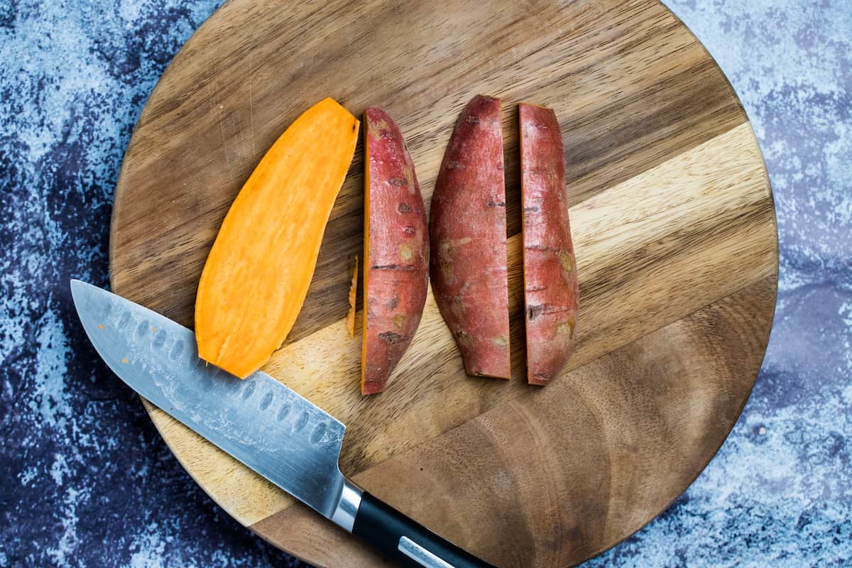 Sweet potatoes cut in half on a cutting board next to a knife.