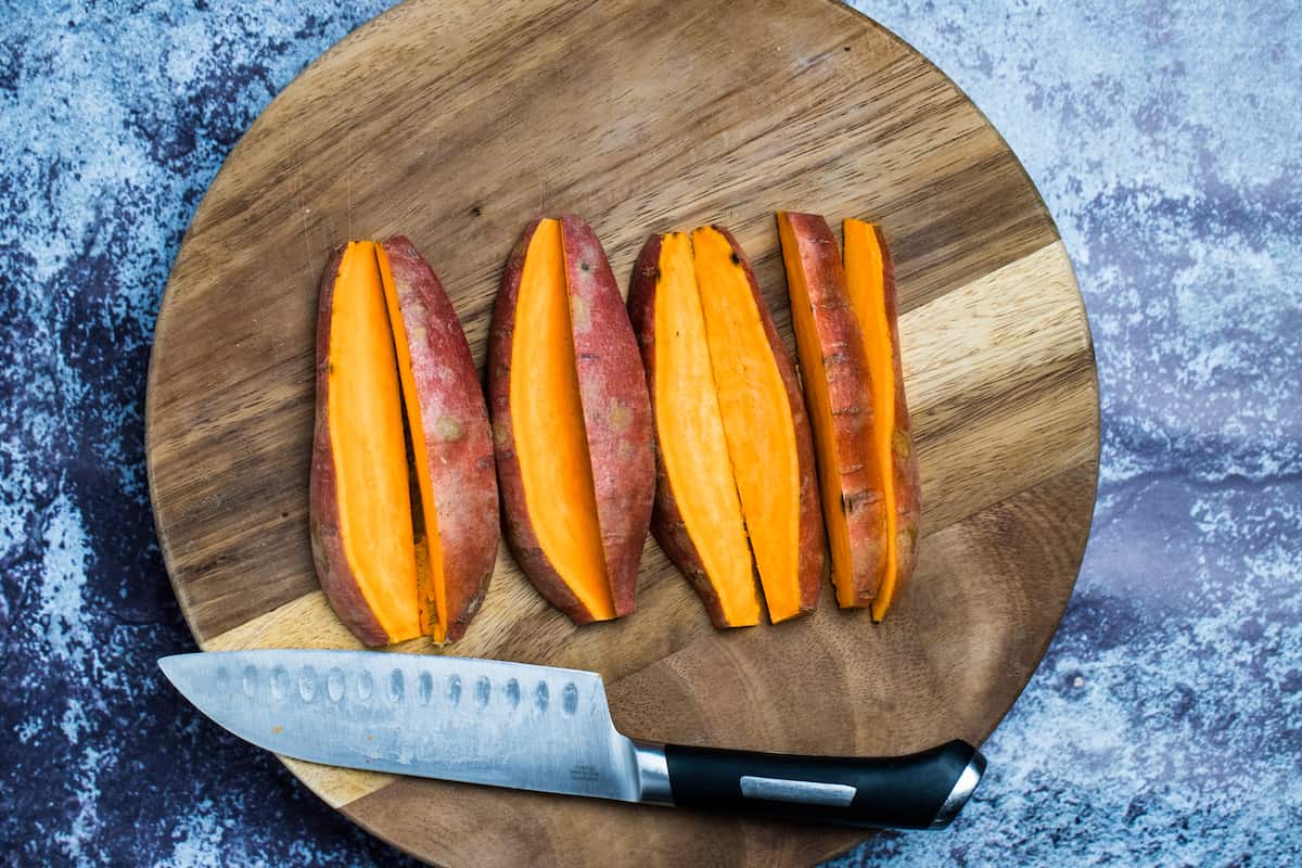 Sweet potatoes cut into wedges on a cutting board next to a knife.