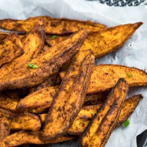 Fully cooked Air Fryer Sweet Potato Wedges sitting on top of parchment paper. They look crispy.