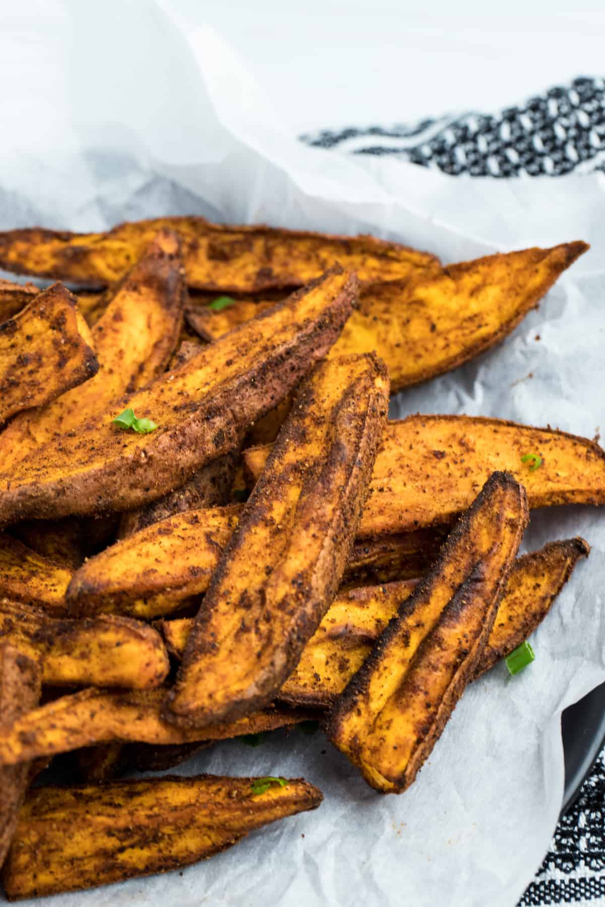 Fully cooked Air Fryer Sweet Potato Wedges sitting on top of parchment paper. They look crispy.