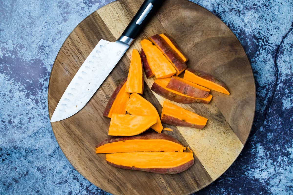 Sweet potatoes cut into wedges on a cutting board.